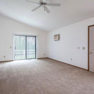 An empty room with a ceiling fan and sliding glass doors, allowing natural light to enter.