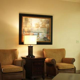 A cozy living room setup featuring two armchairs, a central lamp on a side table, and a large framed artwork on the wall.