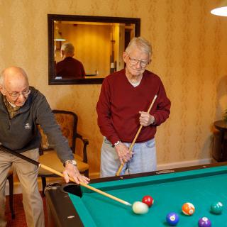 Two seniors playing a game of billiards together indoors.
