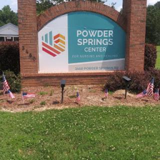 Sign at the Powder Springs Community Center, surrounded by flags in a landscaped area.