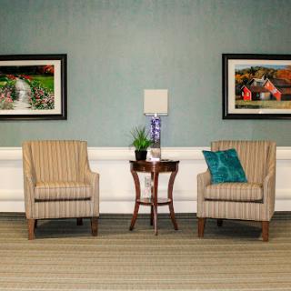 A cozy seating area featuring two striped chairs, a small table with a plant, and framed artwork on the walls.