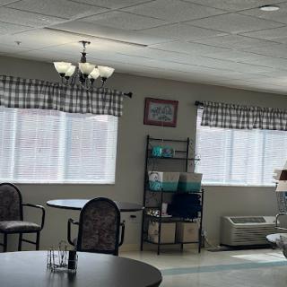 A cozy interior space featuring tables and chairs, with natural light filtering through checked curtains.