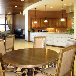 A spacious open-plan area featuring a dining room with a round wooden table and chairs, leading into a well-lit kitchen with pendant lights.