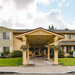 A residential building with a covered entrance and manicured landscaping under a partly cloudy sky.