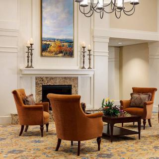 A cozy seating area with armchairs around a fireplace, adorned with artwork and a chandelier.