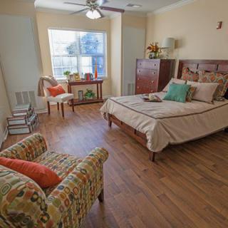 A cozy bedroom with a wooden floor, featuring a bed, chairs, and a large window.
