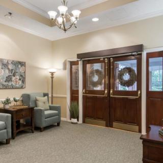 A cozy living room with comfortable chairs and elegant decor, featuring a chandelier and floral artwork.