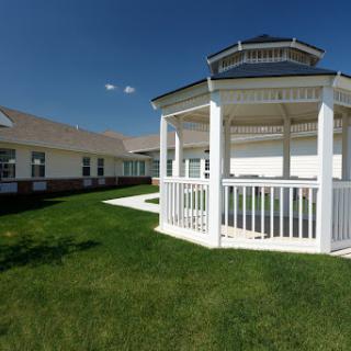 A beautifully designed gazebo surrounded by lush green grass under a clear blue sky.