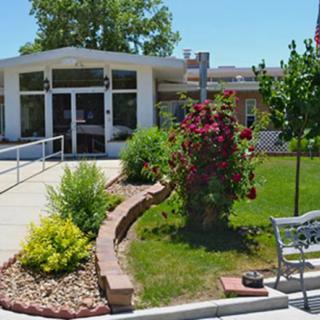 A well-maintained garden leads up to the entrance of a building, featuring vibrant flowers and a stone pathway with a bench nearby.