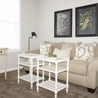 A cozy living room with a beige sofa, white coffee tables, and framed artwork on the wall.