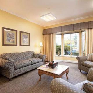 A cozy living room with a sofa, armchairs, and a coffee table, featuring large windows with curtains.