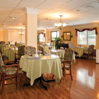 A spacious dining room with elegantly set tables and chairs, featuring chandeliers and a hardwood floor.