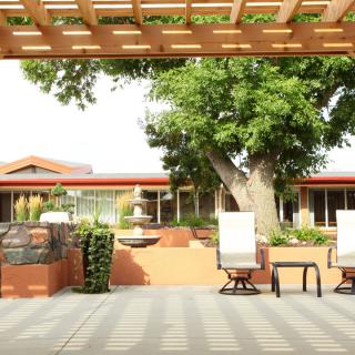 A tranquil outdoor patio setup with comfortable chairs under a wooden pergola, surrounded by greenery.