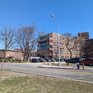 A view of a multi-story building surrounded by bare trees and a parking area under a clear blue sky.
