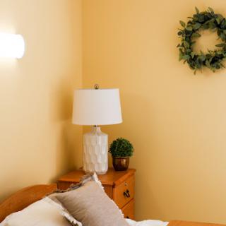 A cozy bedroom setup featuring a lamp and decorative elements against a warm yellow wall.