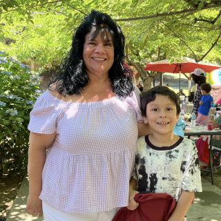 A woman and a child smiling outdoors in a sunny park setting.