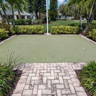A small outdoor putting green surrounded by landscaping and a brick pathway.