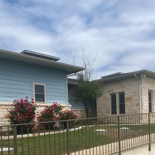 A view of a residential building with a garden and a fence under a cloudy sky.