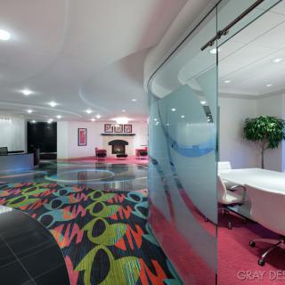 A modern office space featuring a colorful carpet, glass-walled meeting room, and contemporary decor.