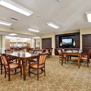 A spacious dining room with multiple tables and chairs, featuring a television and warm lighting.