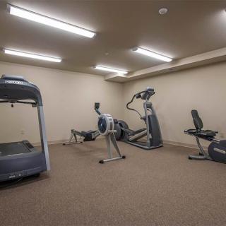 A gym room with various exercise equipment including a treadmill, elliptical, and stationary bike.