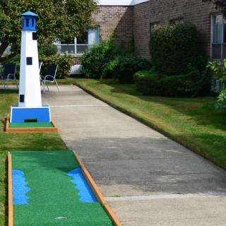 A brightly colored lighthouse marks a hole on a miniature golf course, surrounded by well-maintained grass and pathways.