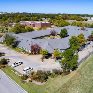 An aerial view of a large building surrounded by trees, with a parking lot and road nearby.