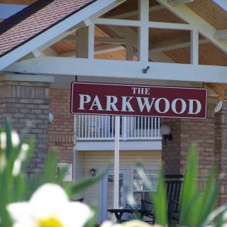 Entrance of a building with a sign reading 'The Parkwood', surrounded by flowering plants.
