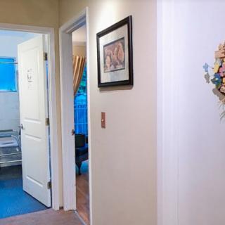 A hallway in a home with open doors leading to a bathroom and bedroom, featuring artwork on the walls.