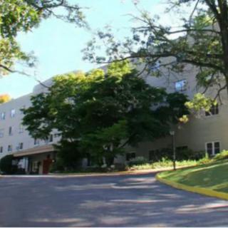 A residential building surrounded by trees with a road in front.