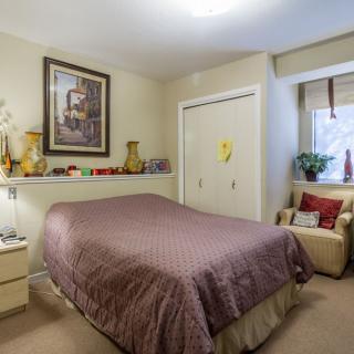 A cozy bedroom with a neatly made bed, decorated with artwork and warm lighting.