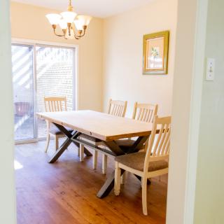 A bright dining room featuring a wooden table and chairs, with a chandelier overhead and a sliding glass door on the side.