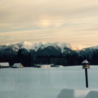 A serene winter landscape with snow-covered fields and mountains under a cloudy sky.
