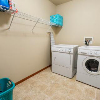 A tidy laundry room featuring a washing machine and dryer, with storage space and cleaning supplies organized on shelves.