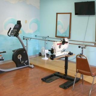 A small indoor rehabilitation room with exercise equipment, including a stationary bike and parallel bars.