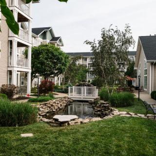 A serene apartment complex with lush greenery, featuring a small pond and bridge.