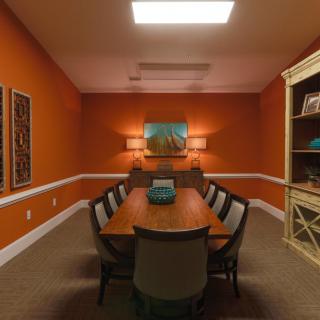 A warm and inviting conference room with orange walls, a long table with chairs, artwork on the wall, and shelves for storage.