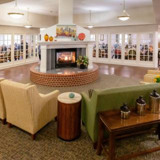 A cozy lounge with comfortable seating arranged around a central fireplace.