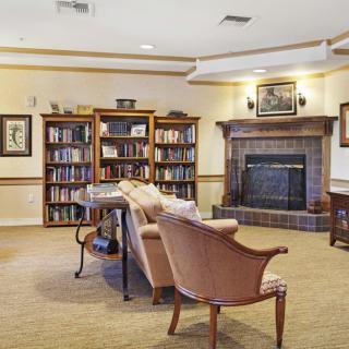 A cozy library room with bookshelves, a fireplace, and comfortable seating.