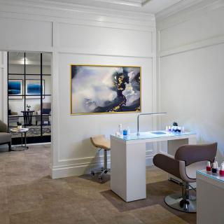 A modern nail salon interior featuring stylish furniture and a large piece of abstract artwork on the wall.