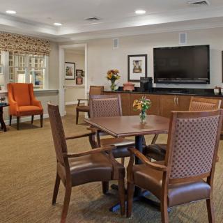 A cozy living room with a dining table and chairs, a large television on the wall, and comfortable seating.