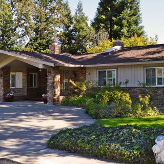 A cozy residential house with a driveway and lush garden surrounded by trees.