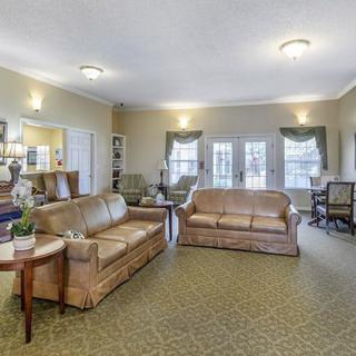 A spacious living room featuring comfortable sofas, a patterned carpet, and large windows letting in natural light.