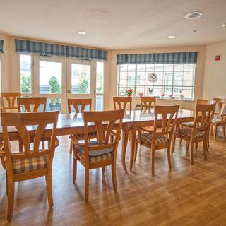 A spacious dining room with wooden tables and chairs, featuring large windows that let in natural light.