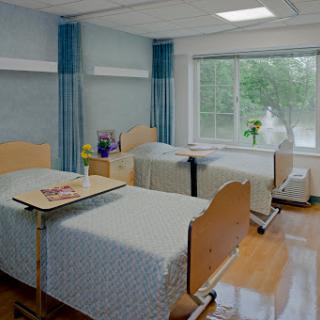 A clean and modern hospital patient room with two beds, a window view, and decorative flowers.