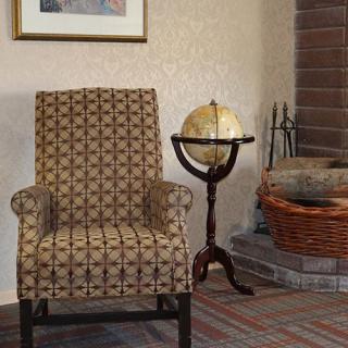 A cozy living room corner featuring an armchair, a globe on a stand, and a fireplace with baskets beside it.