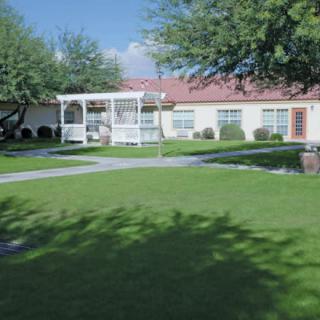 A sunny outdoor area with a well-maintained lawn and a gazebo in front of a building.