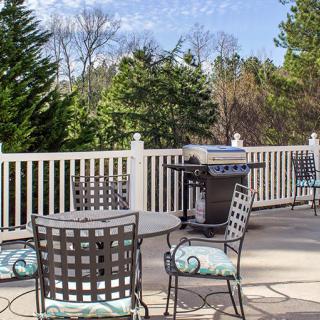 A cozy outdoor patio with metal furniture and a grill, surrounded by nature.
