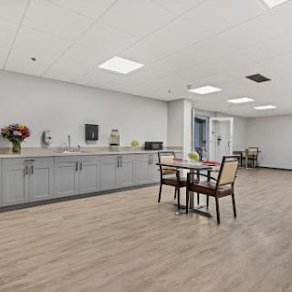 A modern break room featuring a kitchenette, table, and chairs, decorated with flowers.