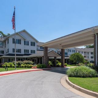 A view of a building entrance with a driveway and landscaping under a clear blue sky.